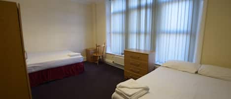 A hotel room with two single beds, a wooden dresser, a chair, and a radiator.