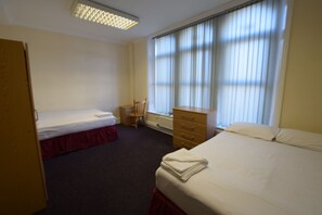 A hotel room with two single beds, a wooden dresser, a chair, and a radiator.