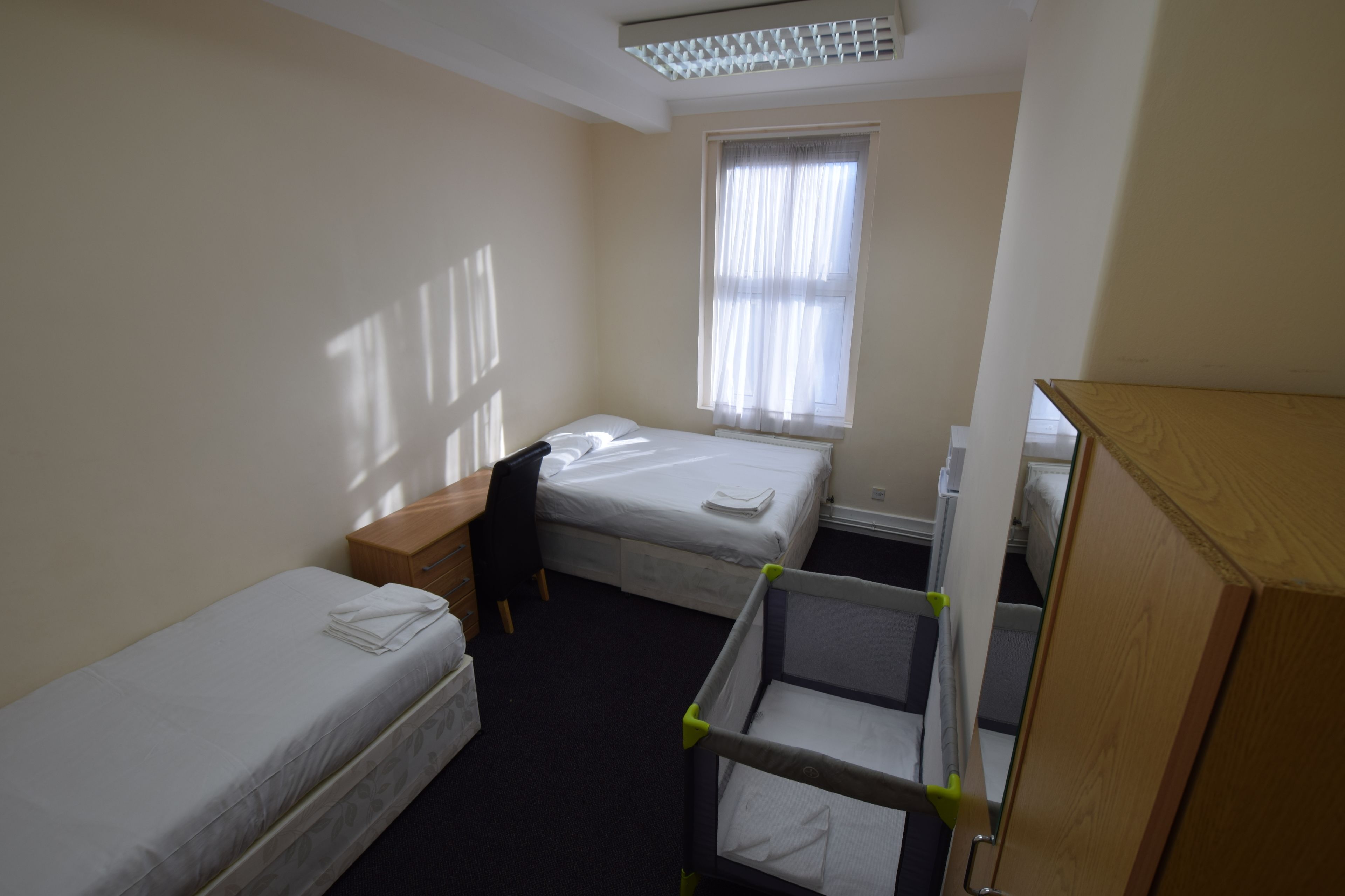 A small, clean room with two single beds, a desk, a chair, and a crib.