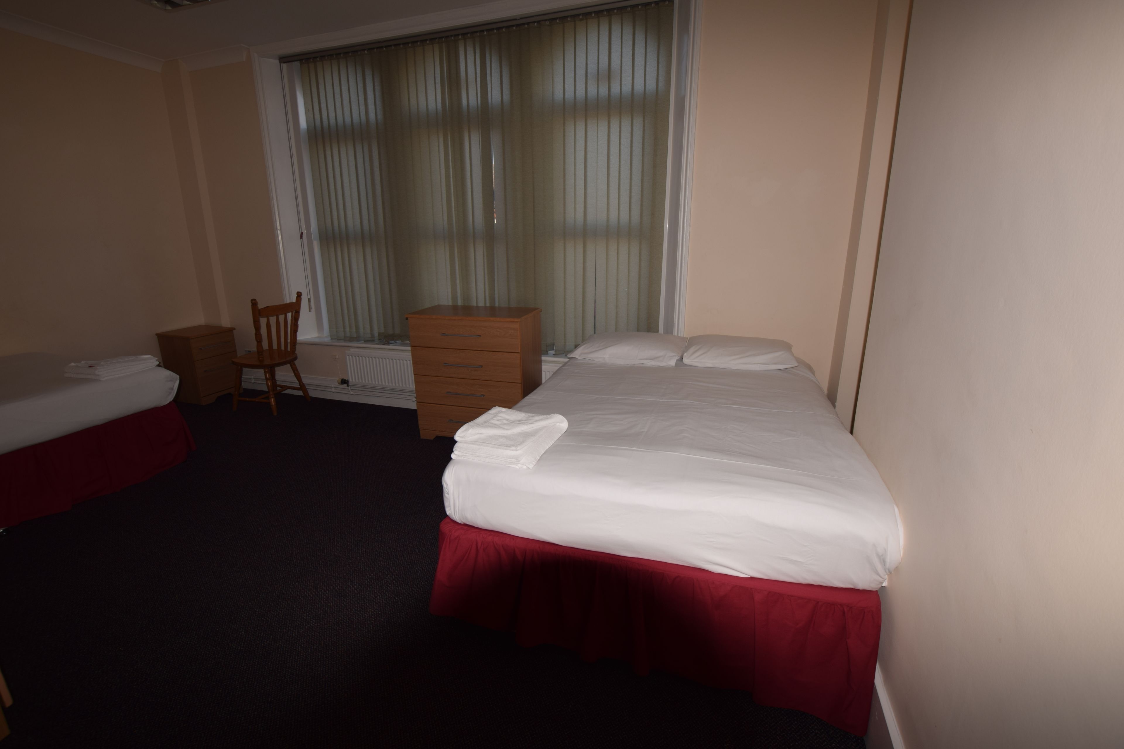 Ein Hotelzimmer mit zwei Betten, einem Holzschrank, einem Sessel und einem Fenster mit Jalousien.