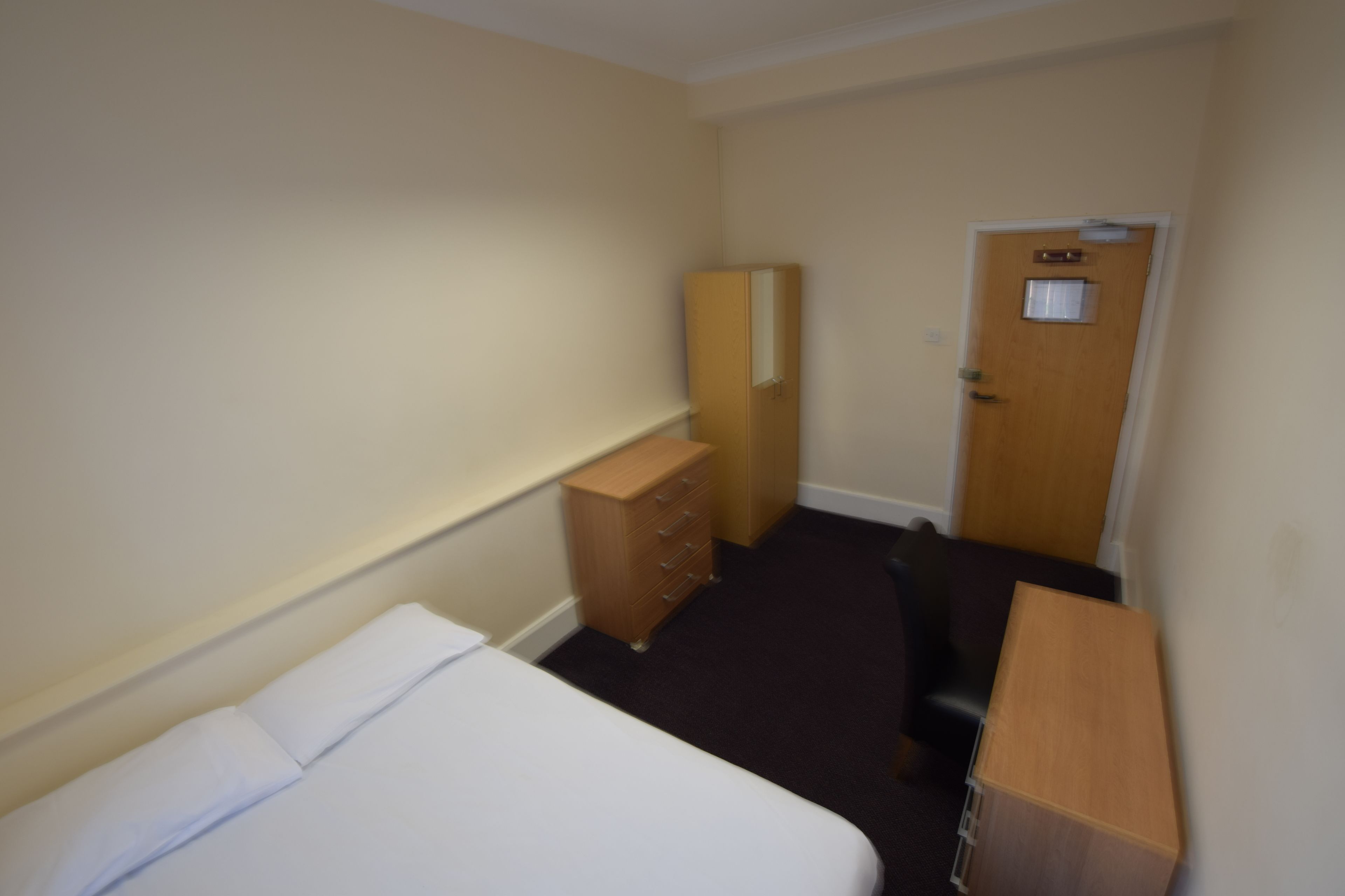 A hotel room with a bed, a wooden dresser, a desk, and a door.