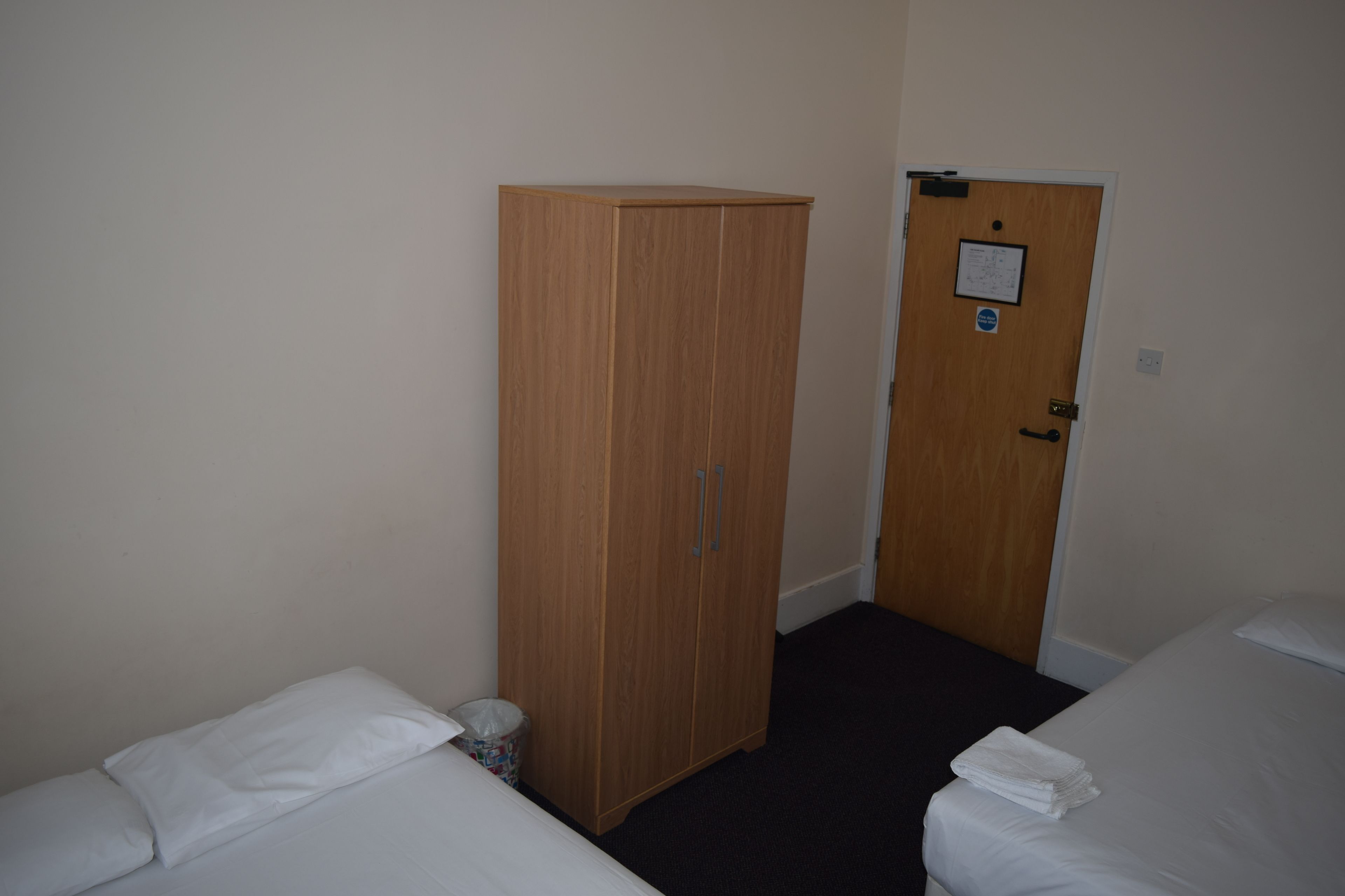 A room with two beds, a wooden wardrobe, and a door with a notice.