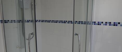 Um chuveiro envidraçado com design curvo, paredes com azulejos brancos e uma faixa azul de azulejos.