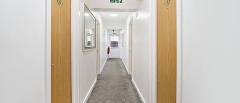 A hallway with wooden doors, a patterned carpet, and a fire exit sign.