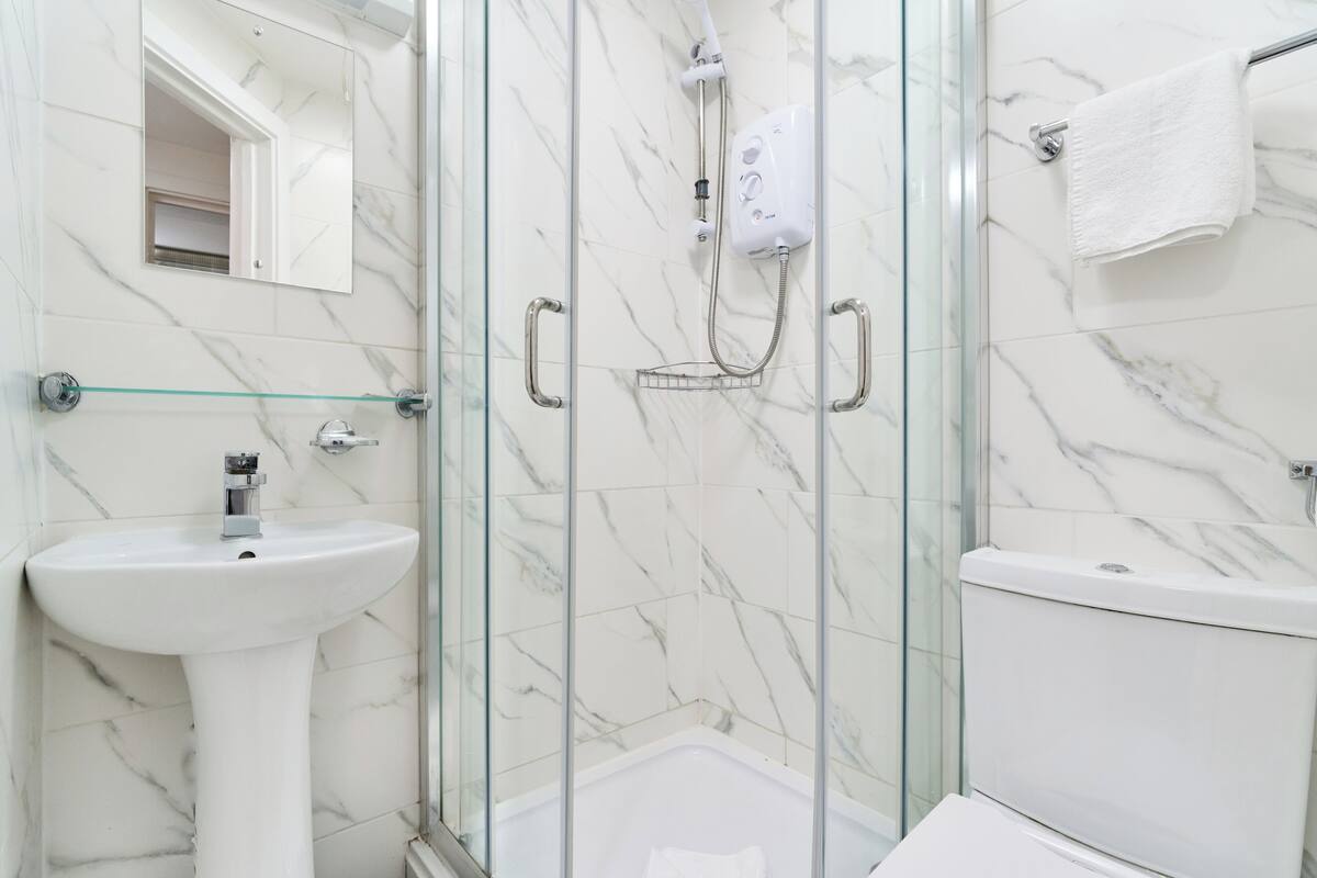 Un baño con ducha de vidrio, lavamanos blanco y un inodoro.