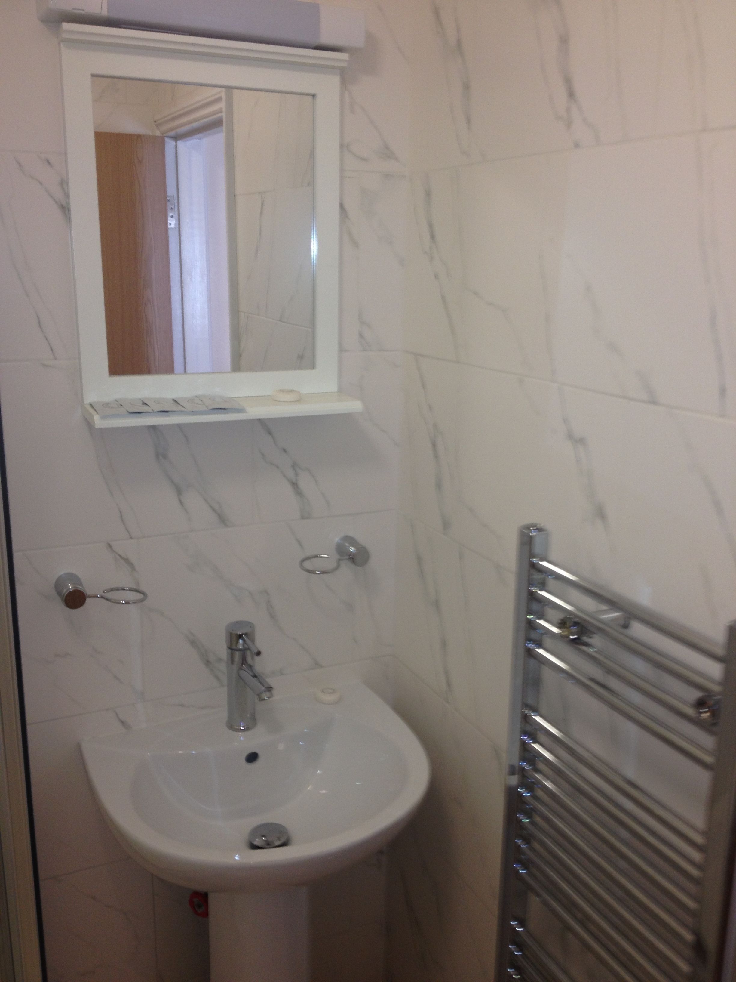 Un baño con un lavamanos de mármol blanco, un espejo y un perchero para toallas.