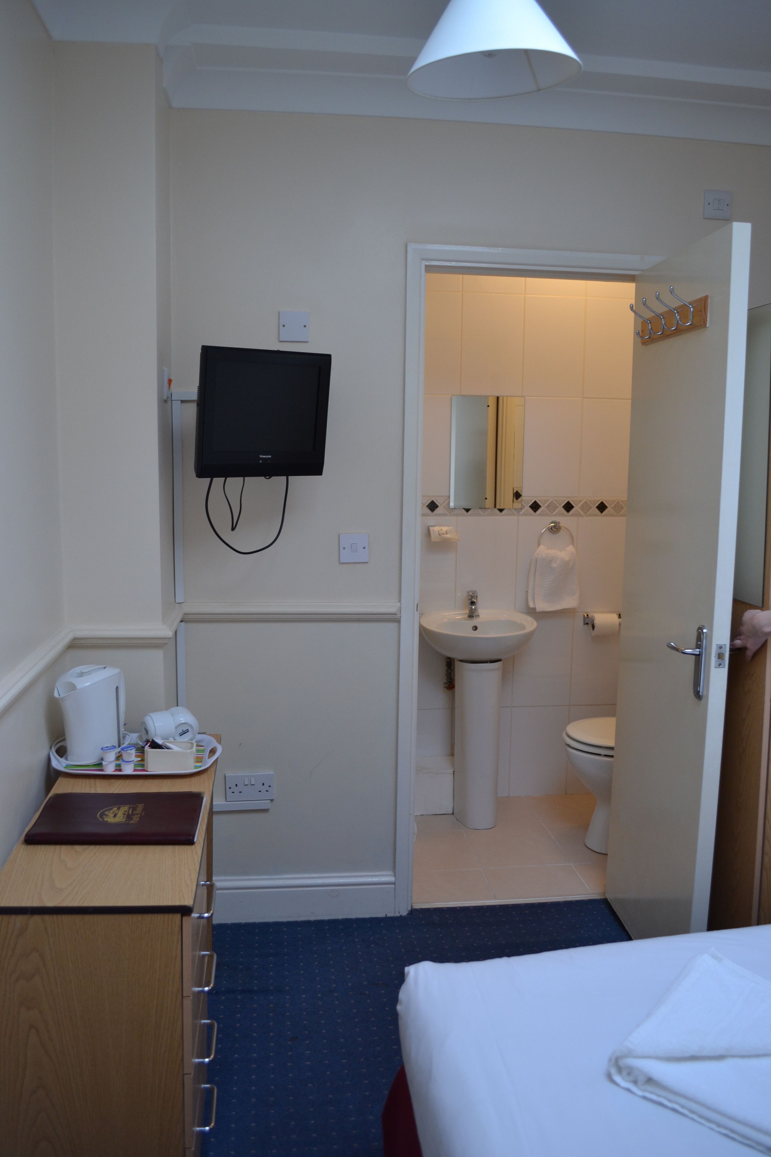 A hotel room with a bed, a desk with a laptop, a TV mounted on the wall, a bathroom with a sink and toilet, and a door leading to another room.