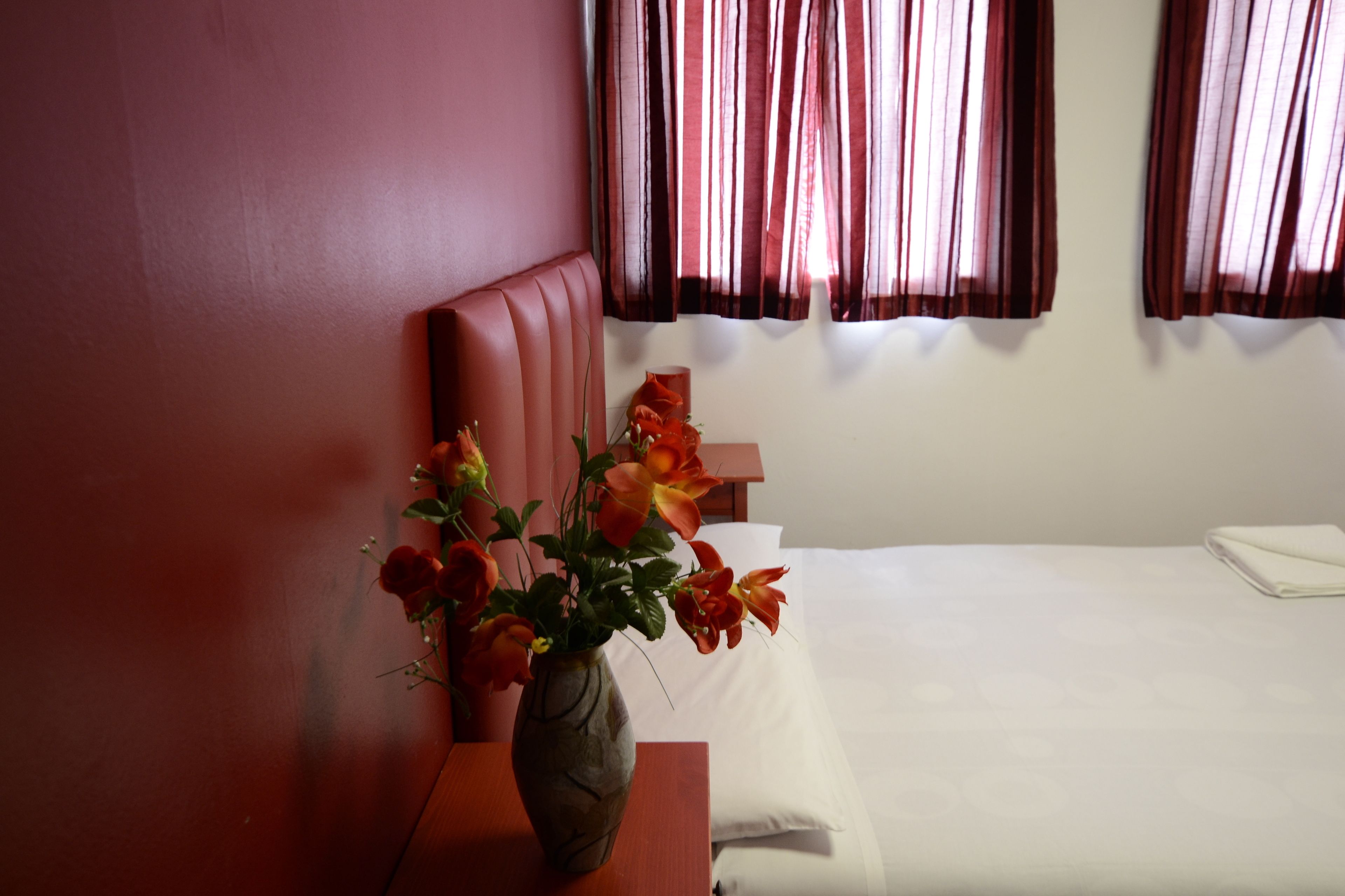A hotel room with a bed, a wooden nightstand, and a vase with flowers.
