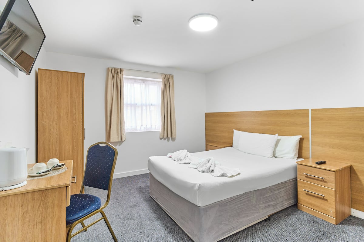 Habitación de hotel con cama, escritorio y silla, televisión y ventana con cortinas.