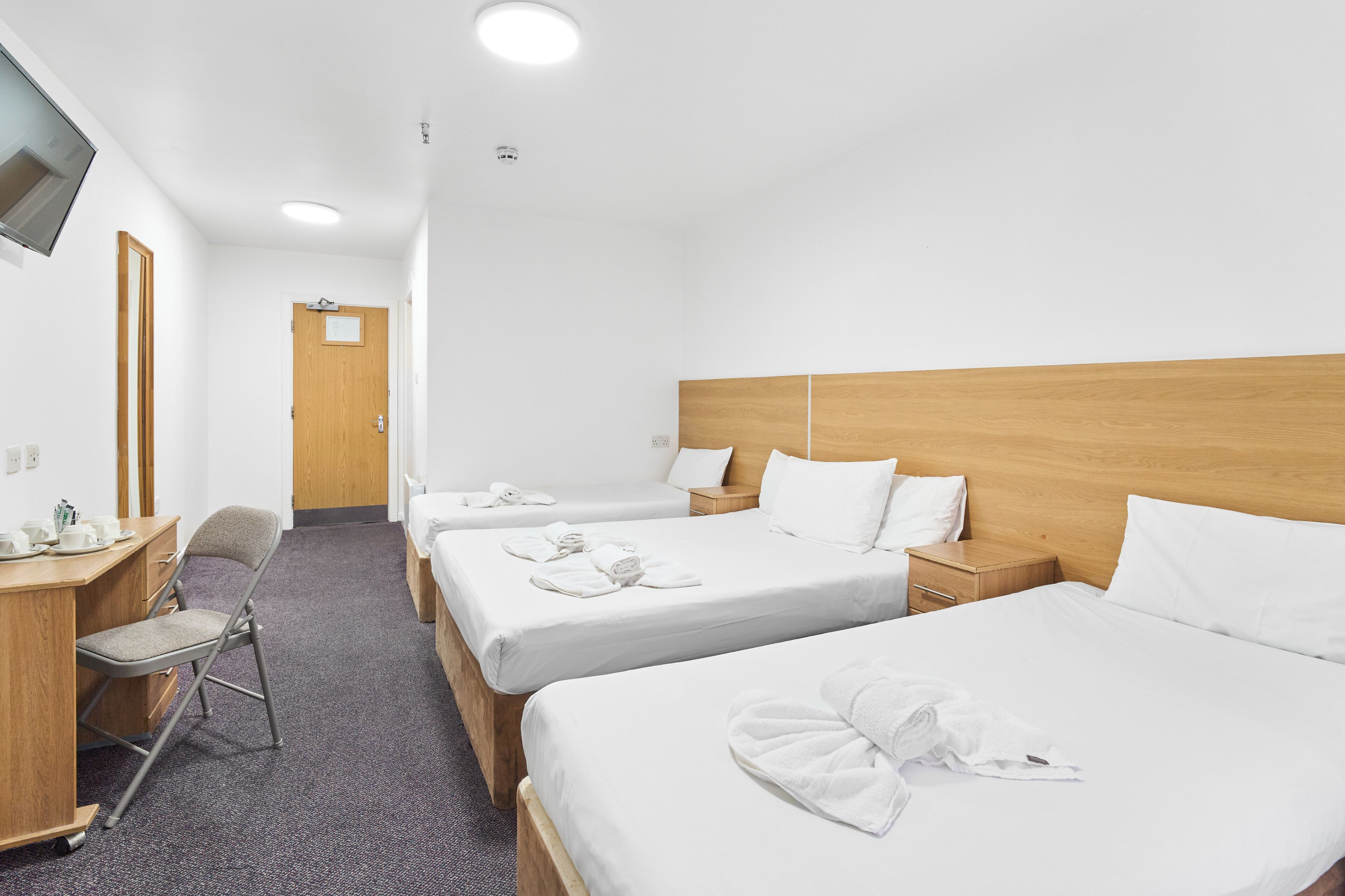 A hotel room with three beds, a desk, a chair, and a TV mounted on the wall.