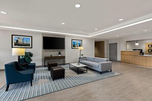 A modern hotel lobby with a sofa, armchairs, a coffee table, and a reception desk.