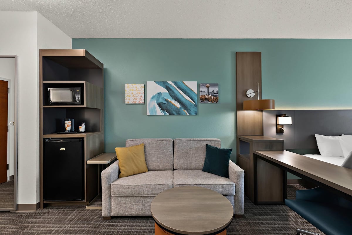 Una habitación de hotel con sofá, una mesita, microondas, refrigerador y obras de arte en la pared.