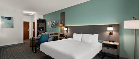 Una habitación de hotel con una cama grande, un escritorio, una silla, una mesita de noche y una lámpara.