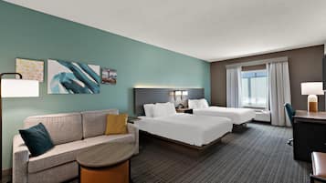 Ein Hotelzimmer mit Bett, Sofa, Schreibtisch und Stuhl. An der Wand hängen zwei Bilder und es gibt ein Fenster mit Vorhängen.