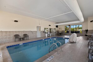 A swimming pool with a blue tiled edge, a covered area, and a view of the outdoors through large windows.