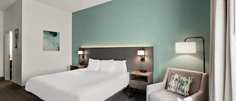 A hotel room with a large bed, a nightstand, a chair, and a wall-mounted lamp.