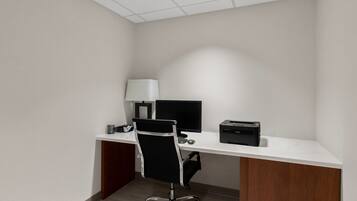 A small office with a white desk, black office chair, two monitors, a printer, and a lamp.
