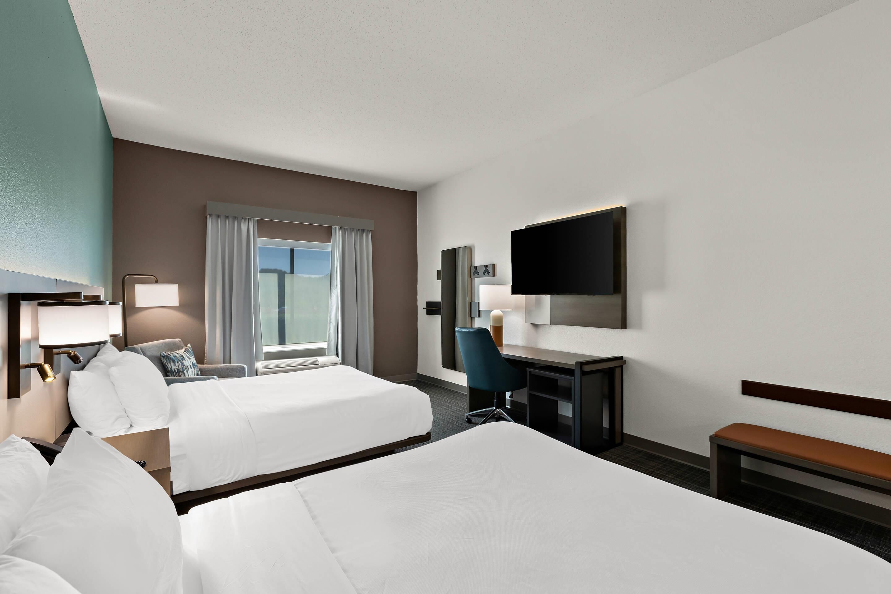 A hotel room with two beds, a desk, a chair, a TV, and a window with curtains.