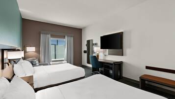 A hotel room with two beds, a desk, a chair, a TV, and a window with curtains.