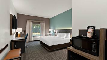 A hotel room with a bed, desk, chair, and a microwave.