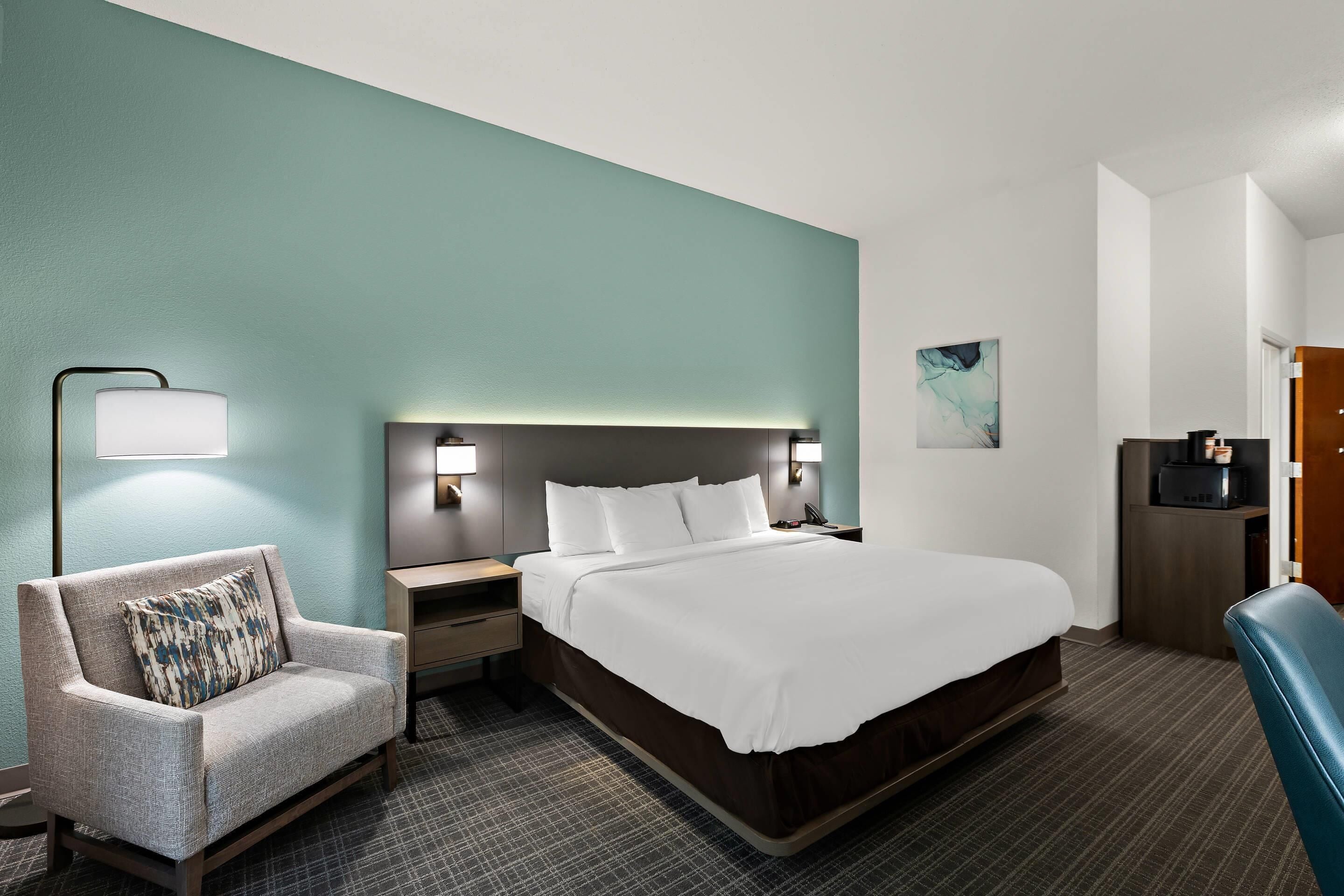 A hotel room with a bed, a chair, a nightstand, a lamp, and a microwave.