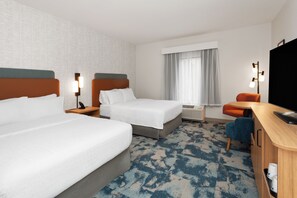 A hotel room with two beds, a desk, a television, and a window with curtains.