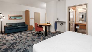 Habitación de hotel con cama, sofá, escritorio con silla, una mesita, un espejo y un cuadro en la pared.