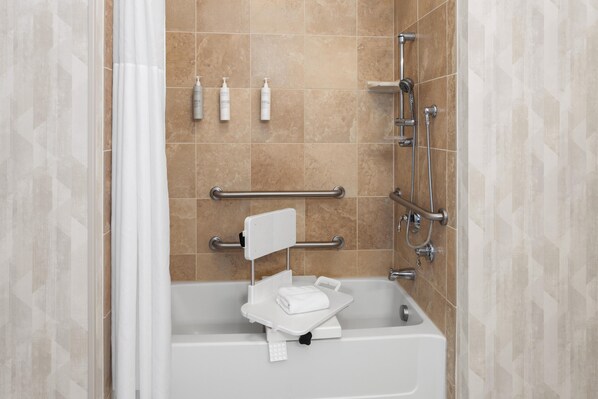 Un baño con bañera, ducha y barras de apoyo. Hay artículos de aseo en la pared.