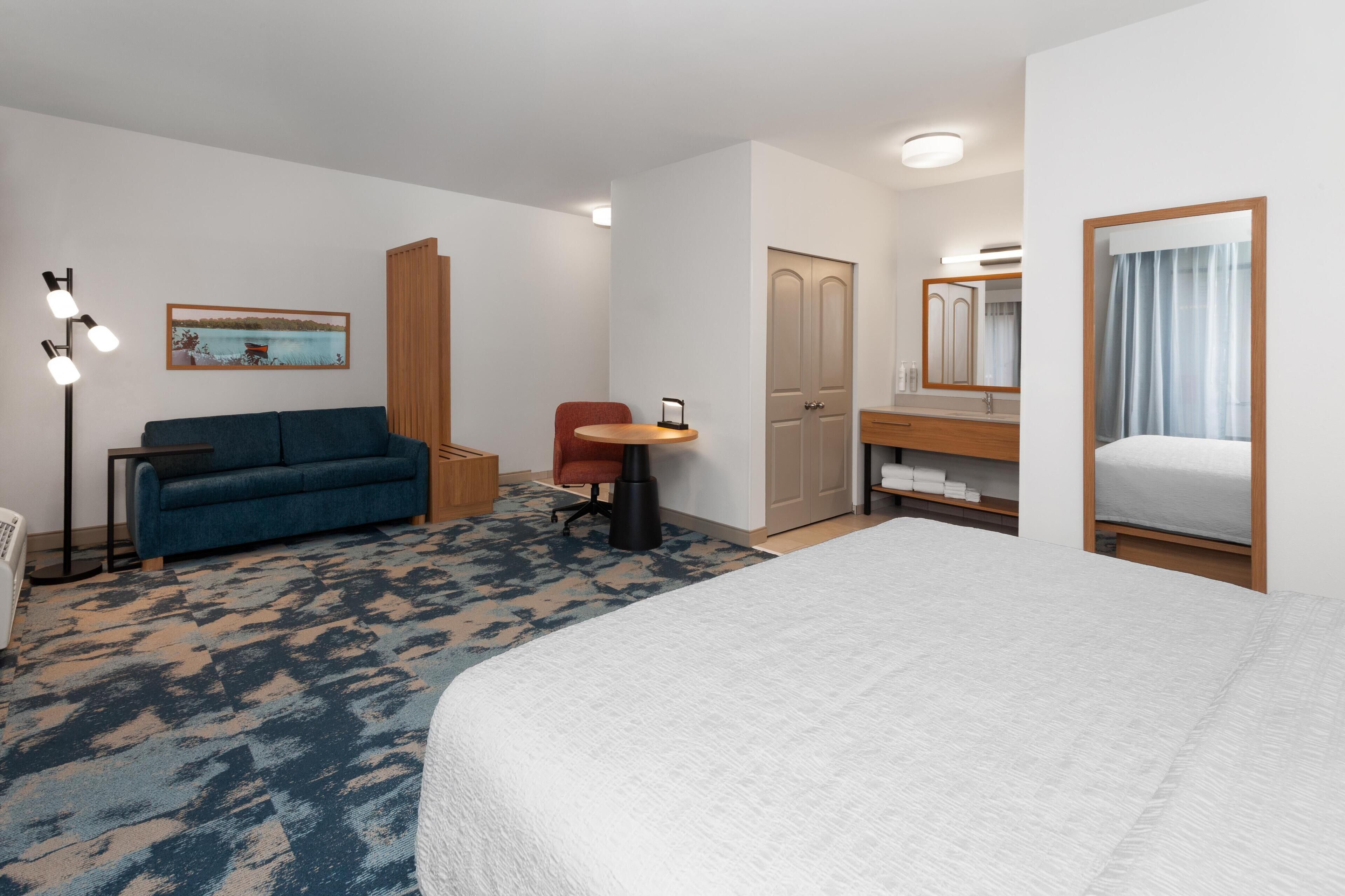 A hotel room with a bed, a sofa, a desk, a chair, a wardrobe, and a mirror.