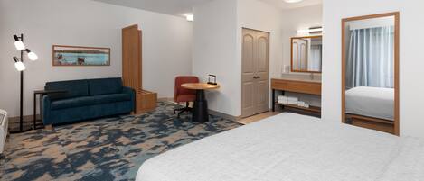 A hotel room with a bed, a sofa, a desk, a chair, a wardrobe, and a mirror.