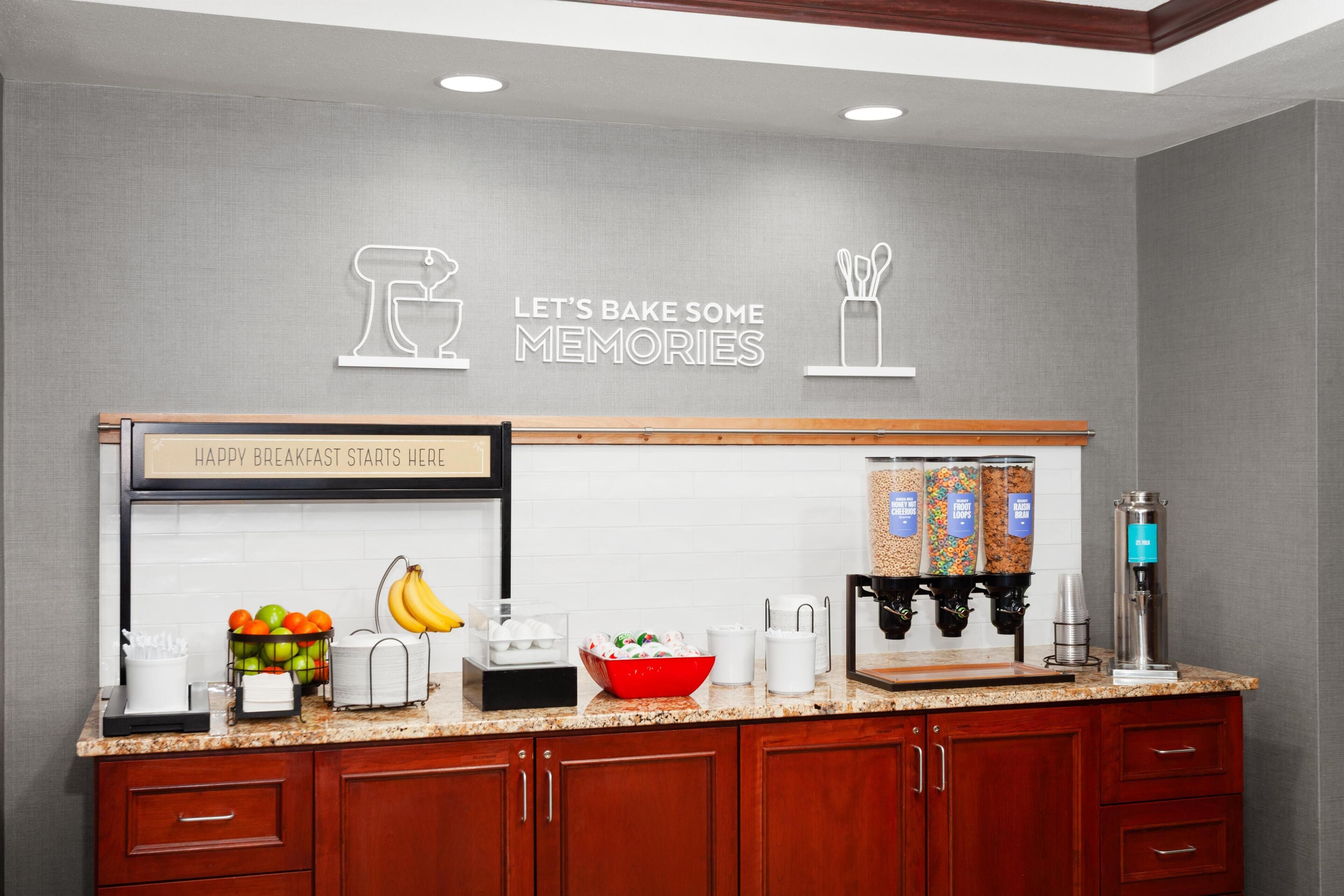Una cocina con barra desayunadora, un cartel que dice 'Happy Breakfast Starts Here', y diversos electrodomésticos y utensilios de cocina.