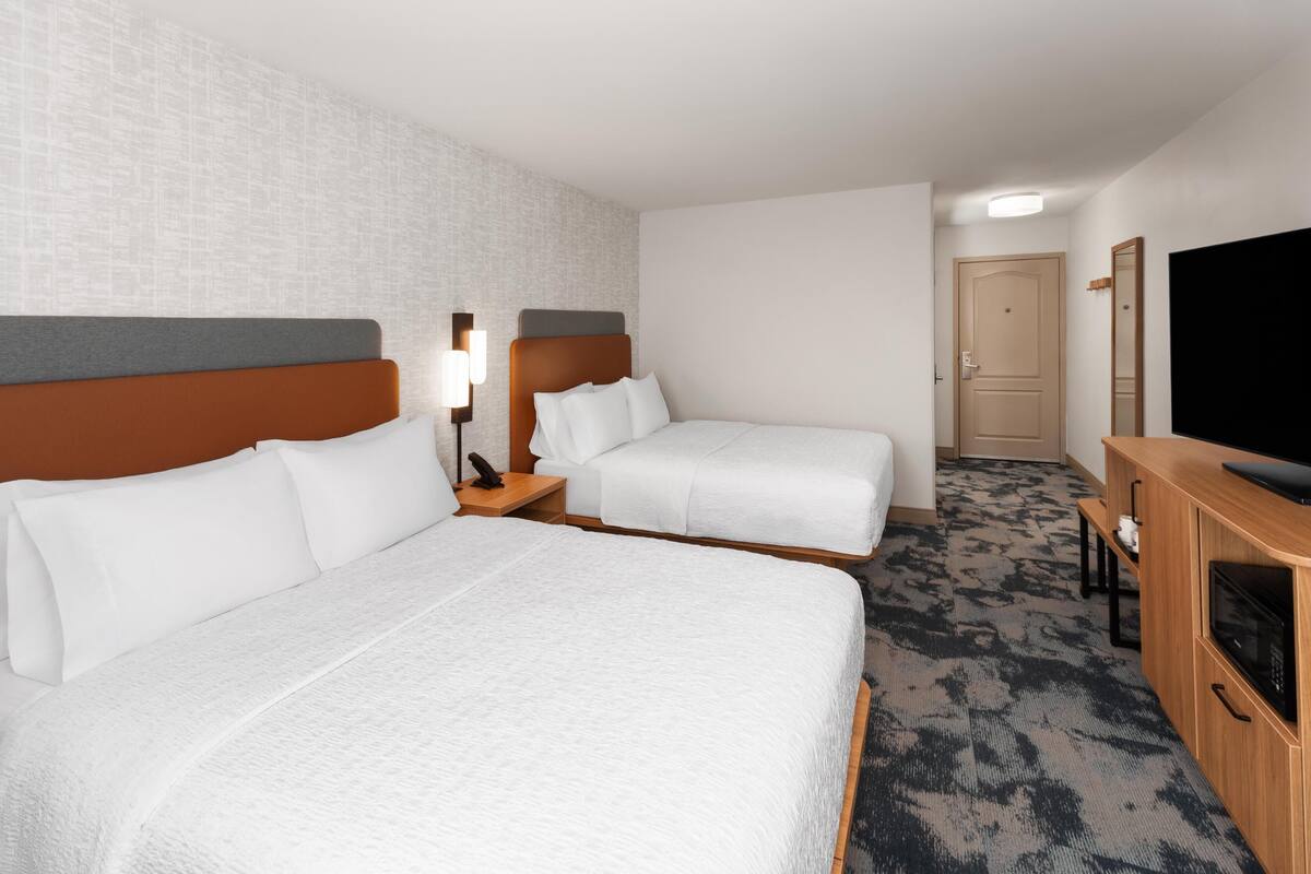 Quarto de hotel com duas camas, uma televisão, uma escrivaninha e um espelho.