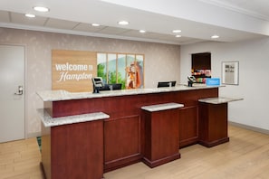 A reception desk with a 'Welcome to Hampton' sign, a computer, and a framed picture on the wall.