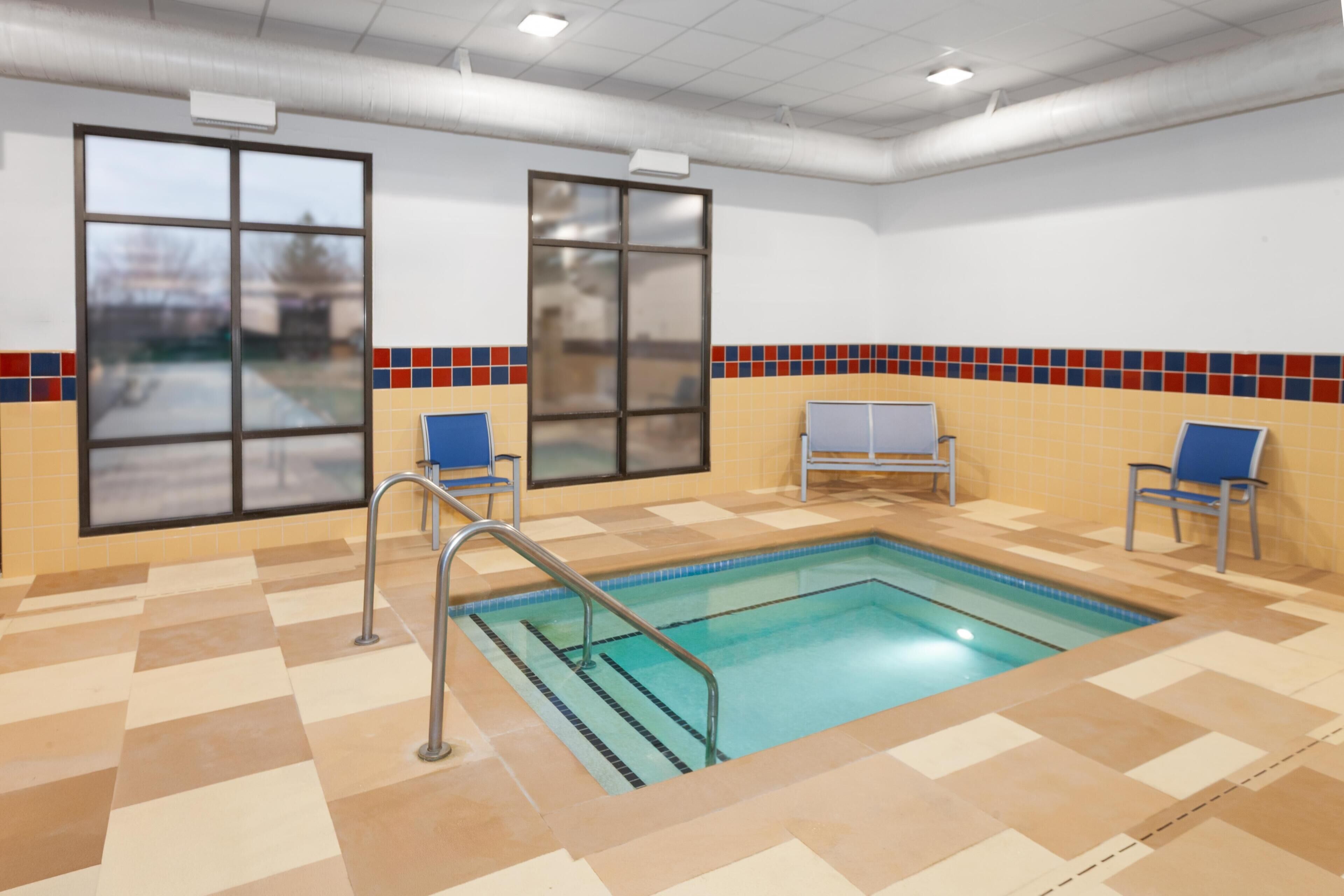 An indoor swimming pool with tiled walls and floor, two windows, and a bench.