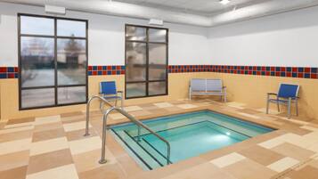 Une piscine intérieure avec des murs et un sol carrelés, deux fenêtres et un banc.