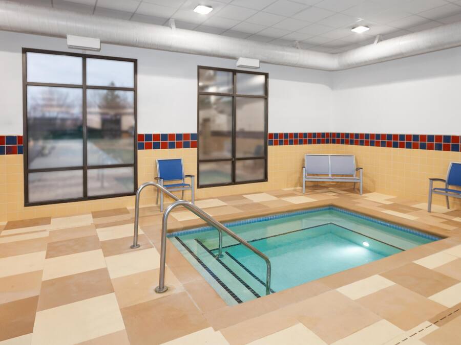 Une piscine intérieure avec des murs et un sol carrelés, deux fenêtres et un banc.