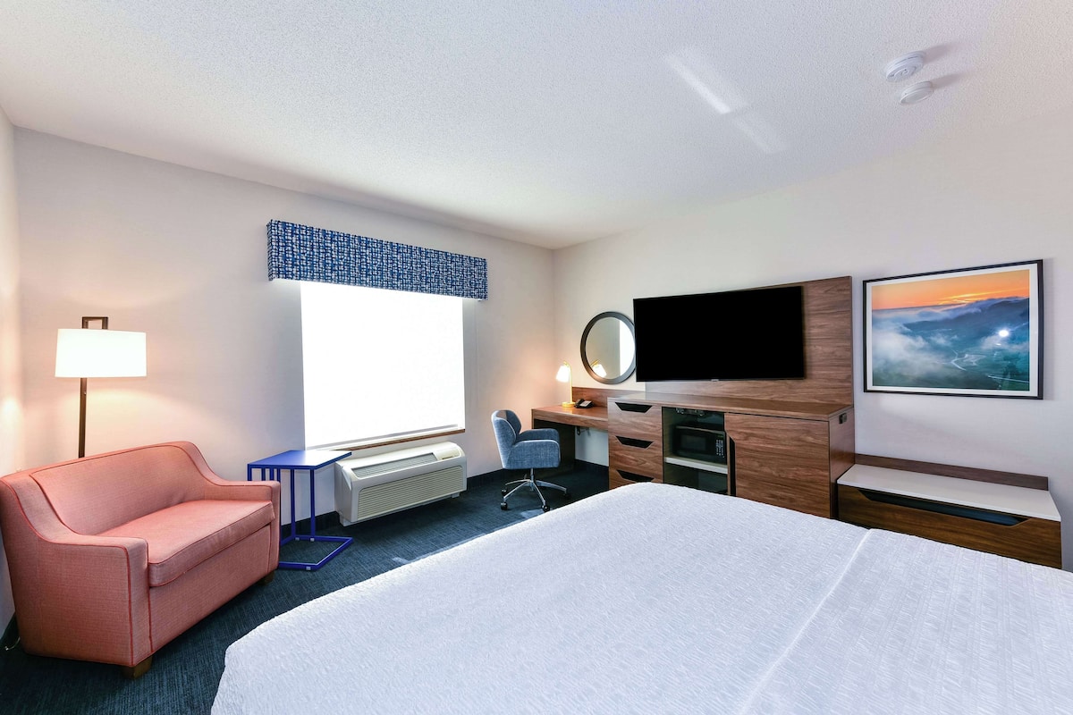 A hotel room with a bed, a desk, a chair, a TV, and a window with a view.