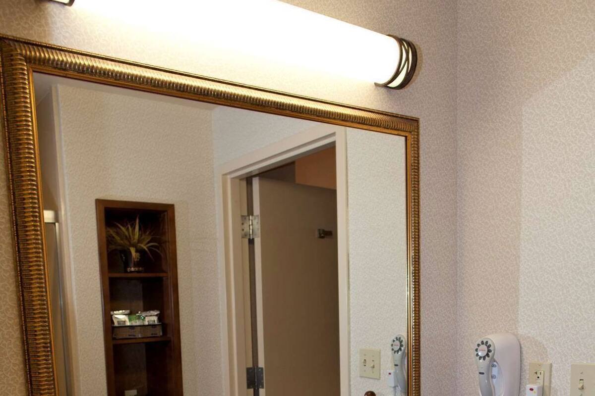 A bathroom with a large mirror, a sink, a towel dispenser, and a hairdryer.