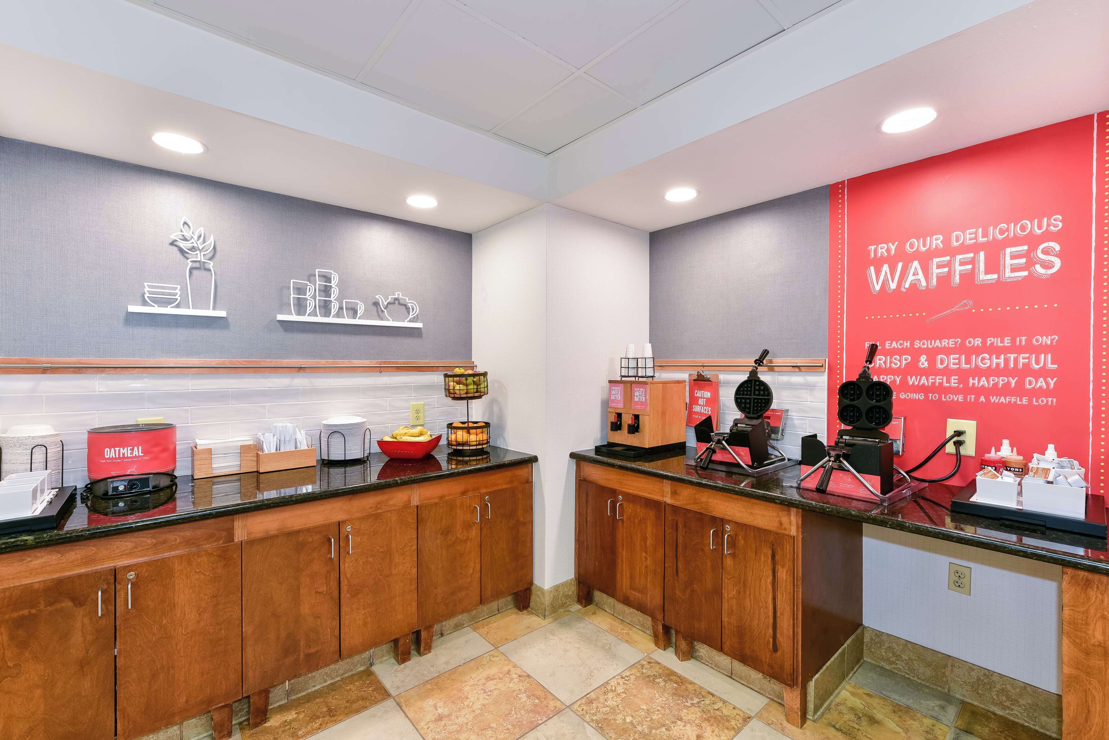 Eine Küchenzeile mit Holzausstattung, einer Arbeitsplatte mit einem Waffeleisen und einer roten Wand mit Werbung für Waffeln.