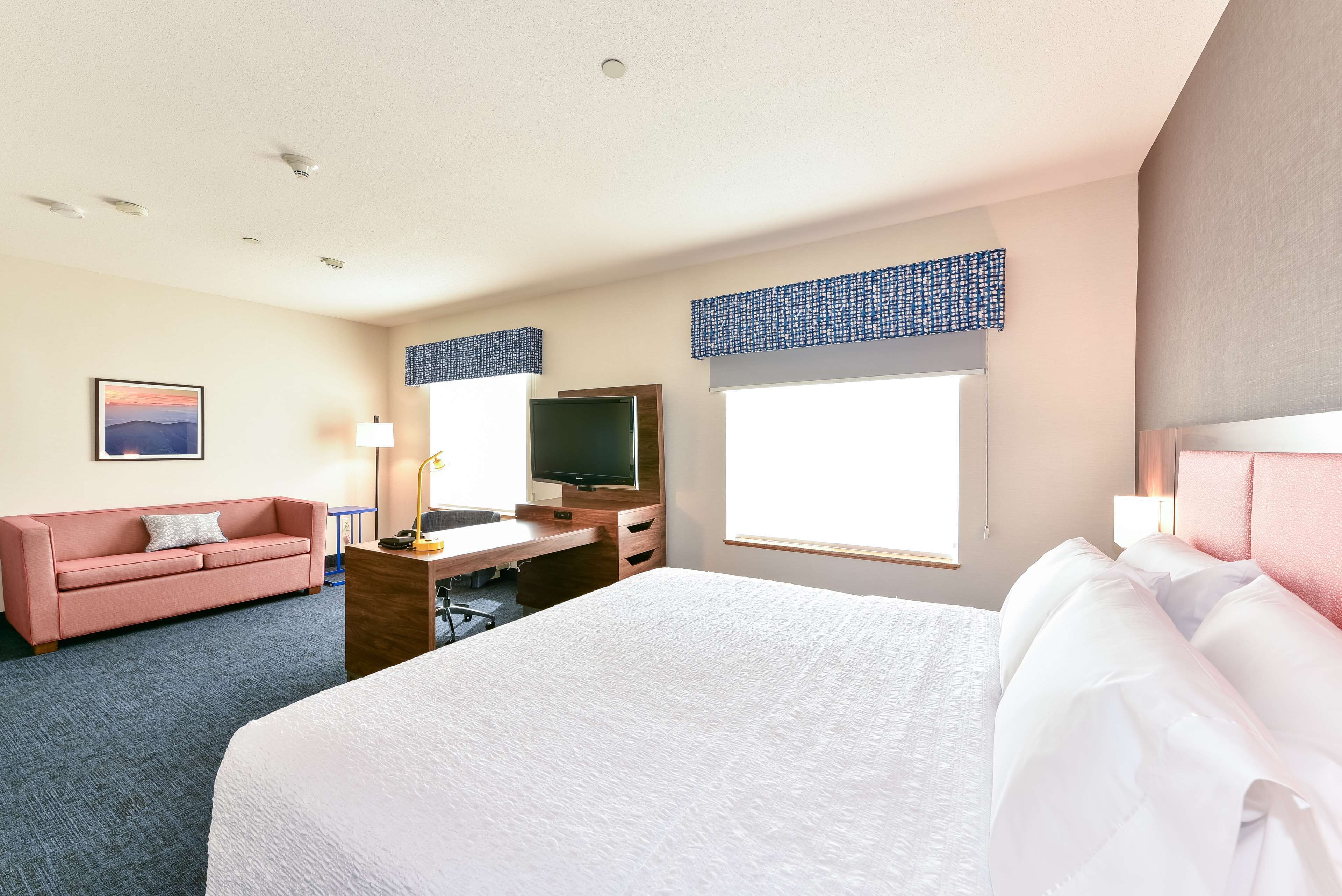 Ein Hotelzimmer mit einem großen Bett, einem Schreibtisch mit Flachbildfernseher, einer Couch und einem Fenster mit Jalousien.