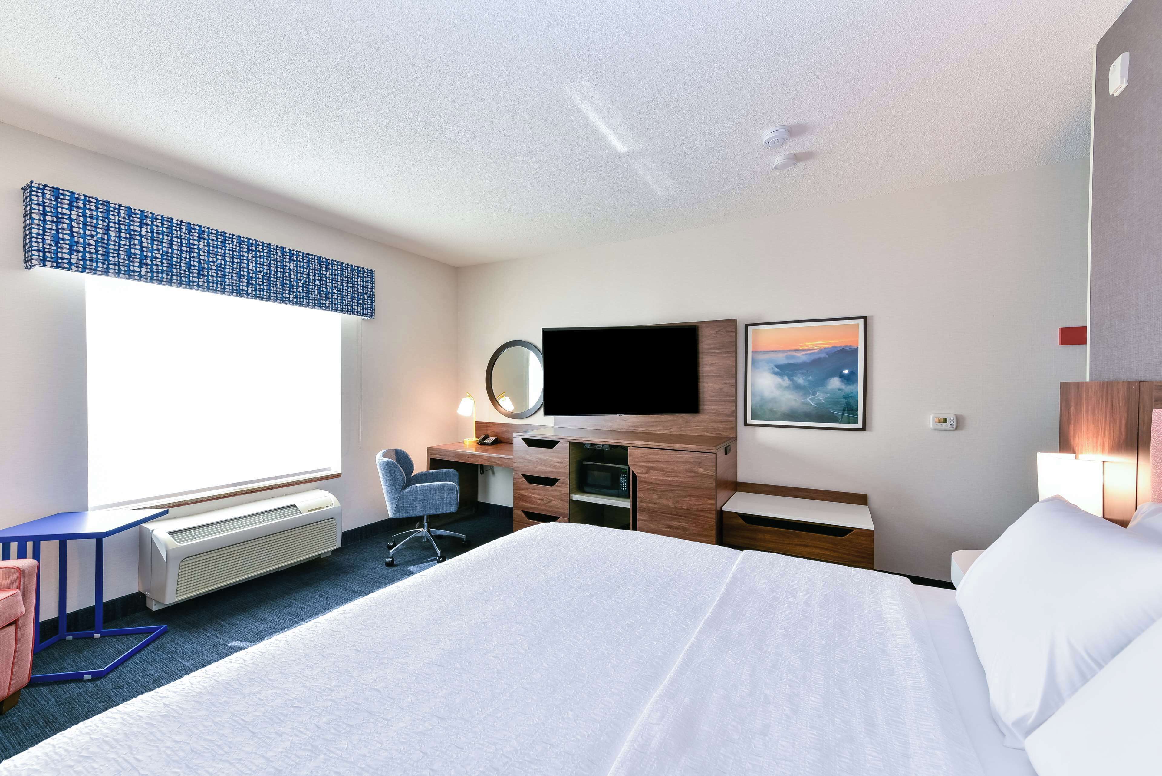 A hotel room with a large bed, a desk with a computer, a TV, and a window with blinds.