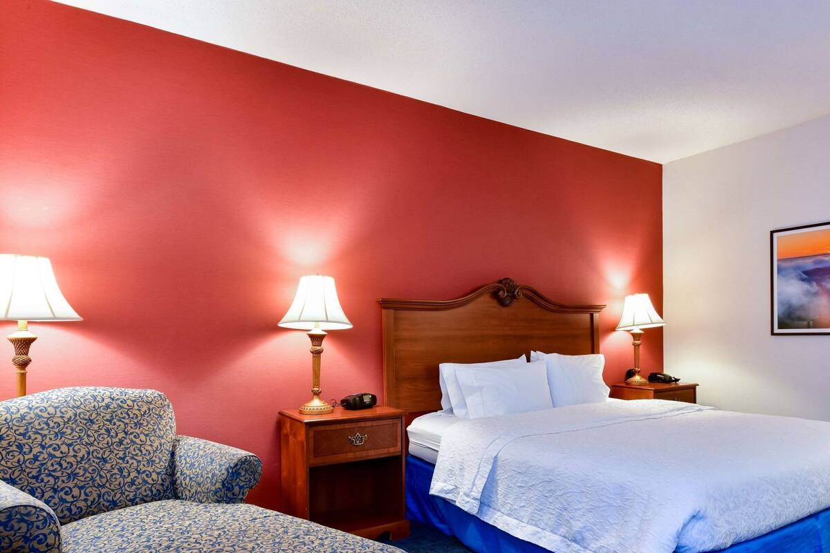 A hotel room with a bed, two bedside tables with lamps, a chair, and a nightstand.