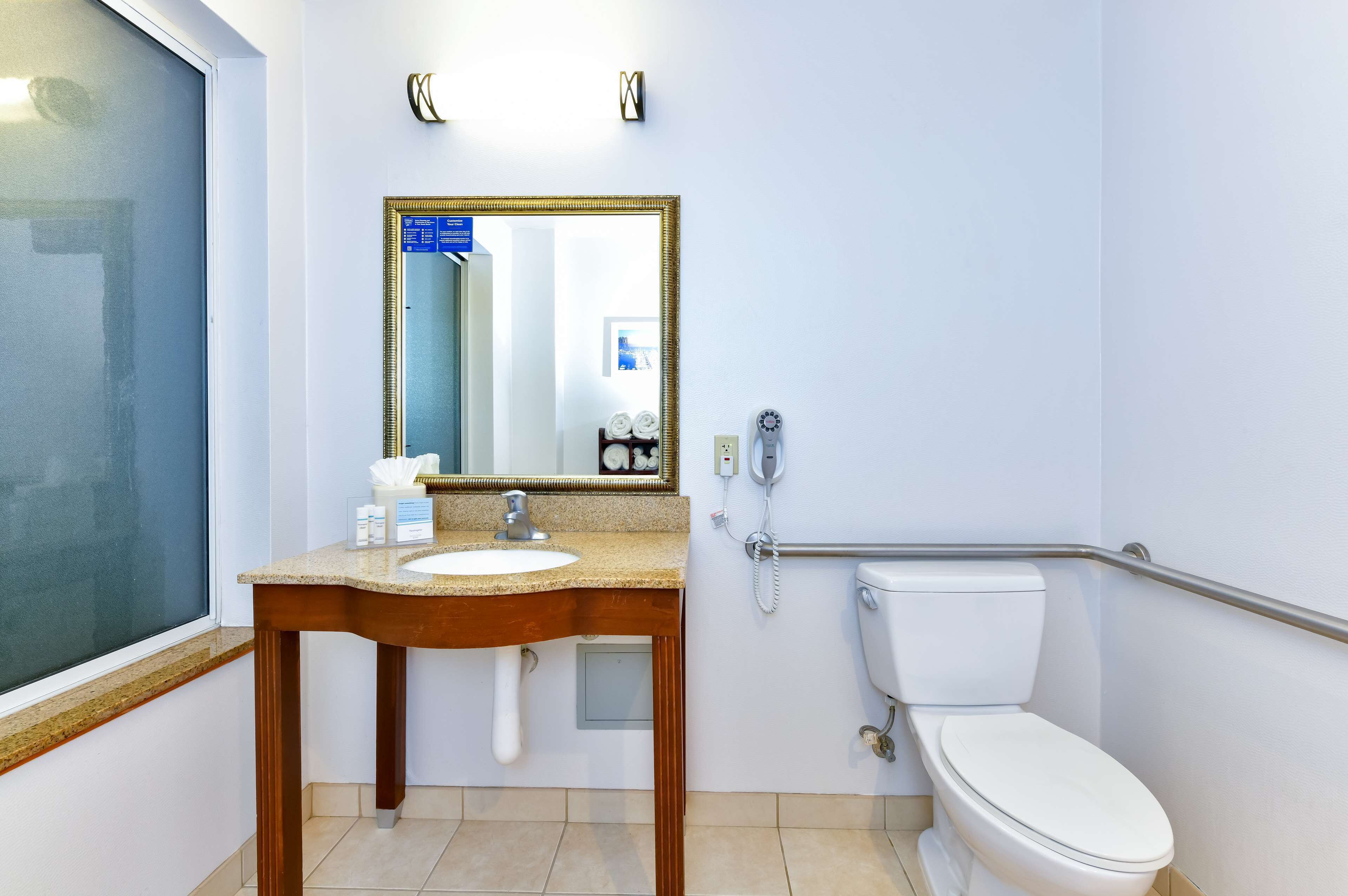 A bathroom with a sink, mirror, toilet, and a handrail.