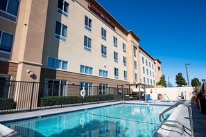 A hotel with a swimming pool, a fenced area, and a clear blue sky.