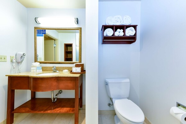 A bathroom with a wooden vanity, a large mirror, a toilet, and a shelf with towels.