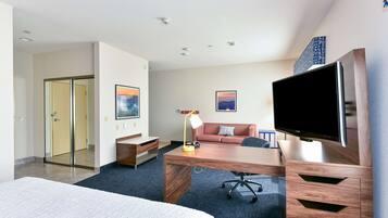 A modern hotel room with a large bed, a desk with a computer, a flat-screen TV, a sofa, and a coffee table.