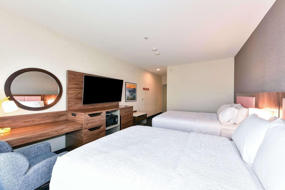 A hotel room with two beds, a TV, a desk with a mirror, and a small seating area.