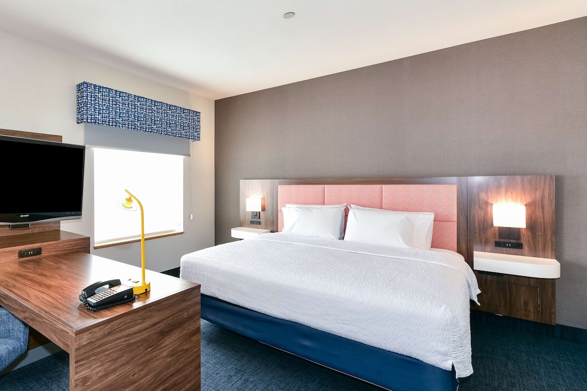 A hotel room with a bed, a desk with a telephone, a television, and two bedside lamps.