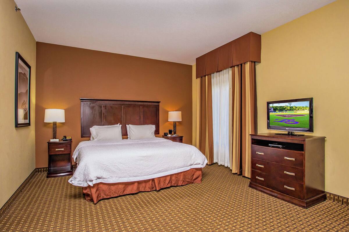 A hotel room with a large bed, two bedside tables with lamps, a dresser, and a television on a stand.