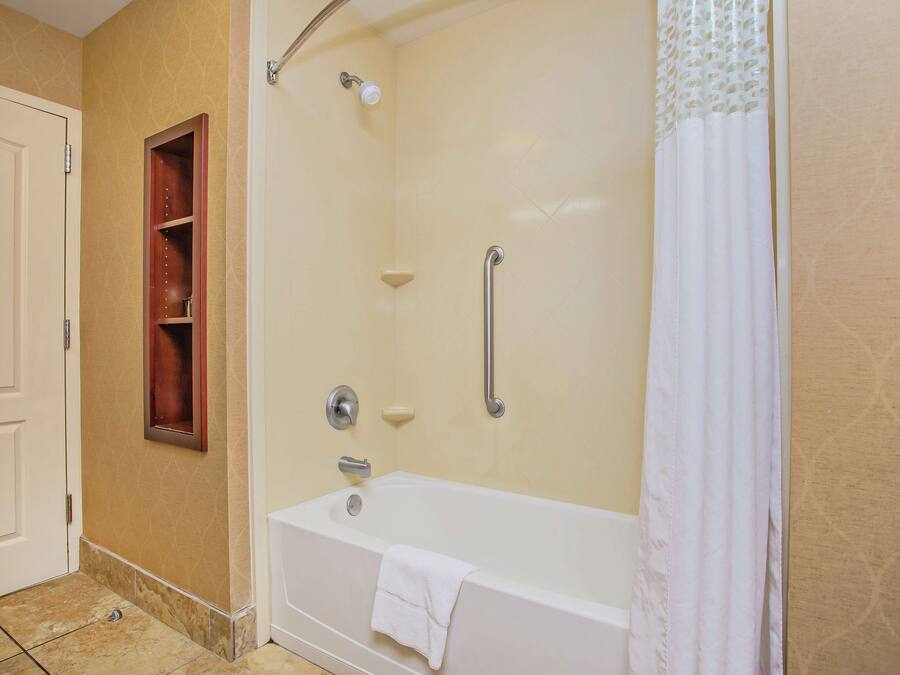 Un baño con una bañera, una ducha con barra de apoyo, una toalla colgada de la bañera y un armario de madera para medicamentos.